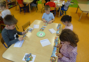 Czwórka dzieci siedzi przy stoliku, każde dziecko układa historyjkę obrazkową.